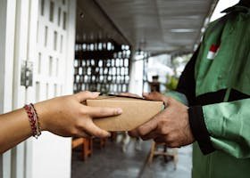 A delivery person hands over a package to a recipient in a close-up view outdoors.